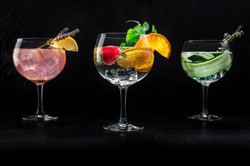 Fancy cocktails with fresh fruit. Gin and tonic drinks with ice at a party, on a black background. Alcohol with lemon, lavender, orange, mint, cucumber