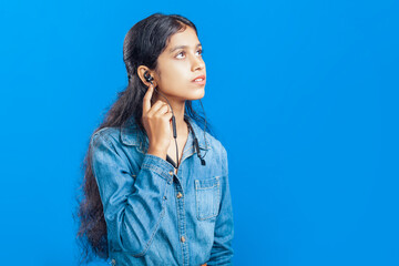 indian teenage girl listening to music on a bluetooth wireless earphone and looking upwards