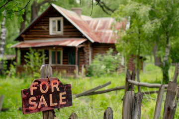 For sale sign in front of old wooden house in the forest.

