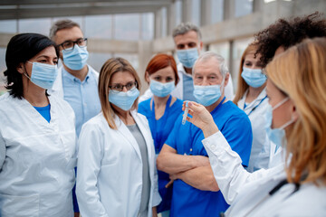 Healthcare team with surgical masks looking at ampule with dangerous virus. Doctors, nurses,...