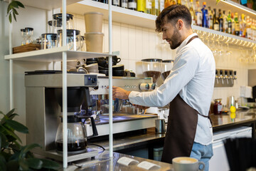 Man in apron preparing coffee via professional machine for customer in cafe