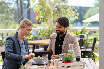 Business lunch for two managers, discussing new business project. Couple sitting outdoors on terrace restaurant, having dinner date.
