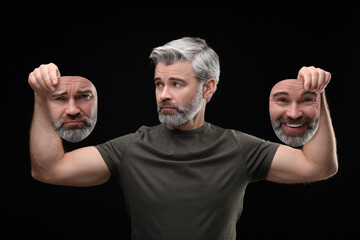 Mature man holding masks with his face showing different emotions on black background. Balanced...