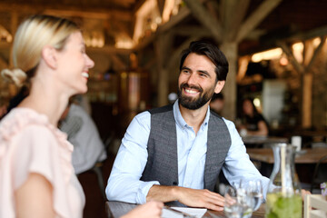 Happy loving couple at date in restaurant. Husband and wife sitting at table, laughing, having lunch in modern cafe.