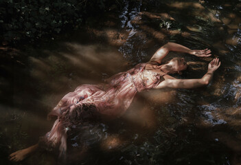 The stretched body of a woman floats on the healing water of the river. Concept of spiritual connection with the natural environment and ethereal atmosphere between two worlds. - obrazy, fototapety, plakaty