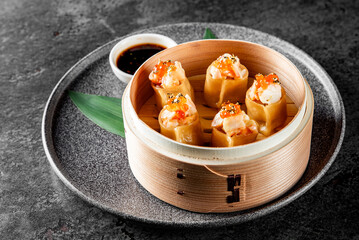 Delicious dim sum in a bamboo steamer, garnished with green onions and roe, served with soy sauce...
