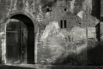 An old textured brick wall with blocked windows and arched doorways in monochrome.