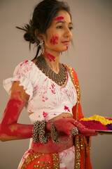 Beautiful young indian woman in traditional dress, holding powder colours in plate, celebrating holi festival. 