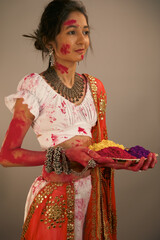 Beautiful young indian woman in traditional costume, holding powder colours in plate, celebrating holi festival.