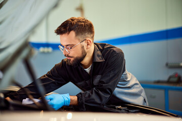 A focused male mechanic technician, working at the repair service shop, checking some car parts. - 761357929