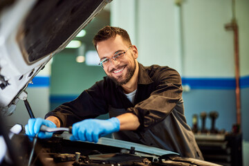 A portrait of a smiling mechanic, posing for the camera, holding and using some tools. - 761358343