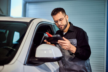Mechanic man working in his garage, using a tablet, and doing a car diagnostic. - 761358973