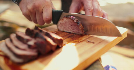 A man is slicing a juicy, freshly cooked steak outdoors.
