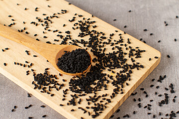 Close-up black sesame seeds in wooden spoon on grey background, organic food concept.