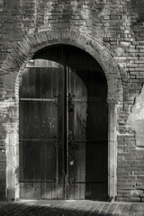 Vertical An old textured brick wall with blocked windows and arched doorways in monochrome.