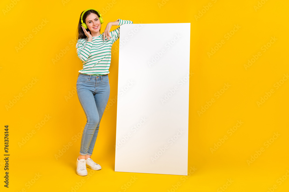 Poster Full body image of cute adorable woman listen music in headset lean on ad placard isolated on yellow color background