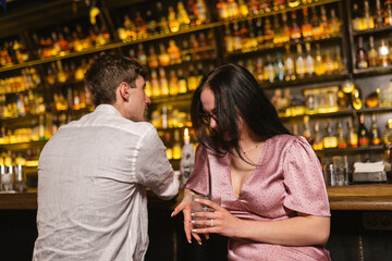 Guy and girl relax and enjoy time near bar counter. Guest near attractive girl looks at various alcoholic drinks on shelves in bar