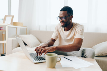 Smiling African American Man Working on Laptop in Modern Home Office, Typing Away in Cyberspace...