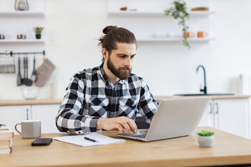 Smiling bearded businessman adult typing on portable computer while working at wooden desk in...