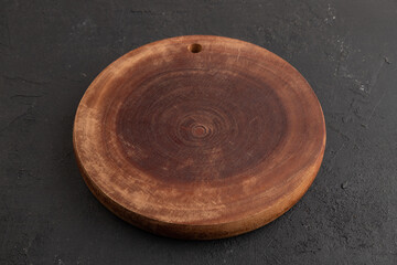 Empty round wooden cutting board on black concrete. Side view