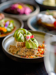 Sourdough toast with avocado beautifully sliced, served with sliced tomatoes on a ceramic plate. Gourmet food. Selective focus.