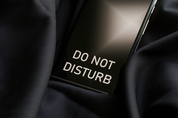Modern smartphone with do not disturb inscription on a dark background made of cozy silk fabric....