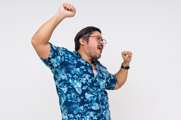 A cheerful and rowdy middle-aged male tourist celebrates by dancing in a vibrant Hawaiian shirt,...