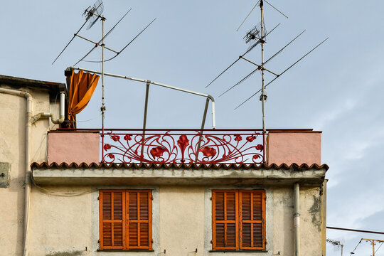 Roof terrace of an old building with red metal railing in Art Nouveau style, TV antennas and closed shutters, Sanremo, Imperia, Liguria, Italy