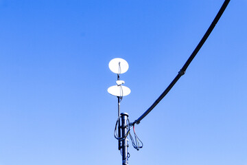 Small satellite dish antenna with wires blue sky, bright sunlight in background. Antenna...