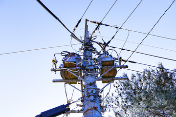 View from below of Transformers small sphere size and electric wire phone lines. Energy and technology. Electrical post on electric power. electrical device. Bright sunny sky and trees in background.