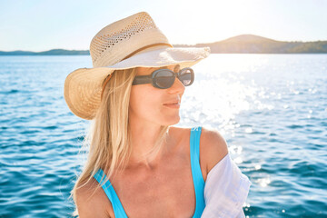 Fashionable beautiful woman relaxing outdoors on the beach on a summer day. I wear a wide-brimmed hat and sunbathe with UV protection. Beach holiday concept.
