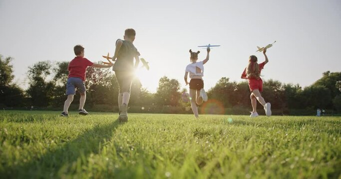 Exhilarated Teens Running with Toy Planes in Evening Sunlight, Embodiment of Summer Joy, Slow Motion