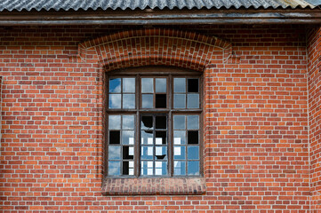 An old window with broken glass panes in a red brick wall
