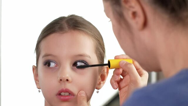 Mother applying makeup to her cute little daughter, close-up