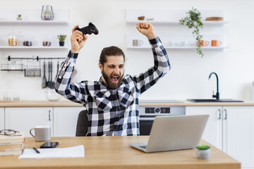 Overjoyed young man in checkered shirt screaming and gesturing while celebrating victory in video...