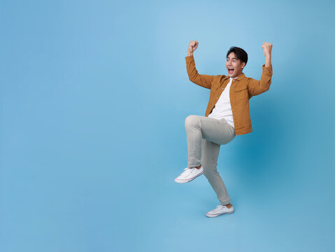 Full body young overjoyed excited happy asian man 20s he do winner gesture isolated on blue background studio portrait. People lifestyle concept