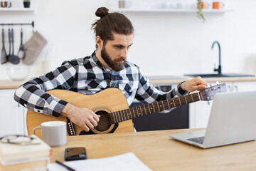 Focused Caucasian male practicing audio exercises on string instrument via online tutorial. Young...