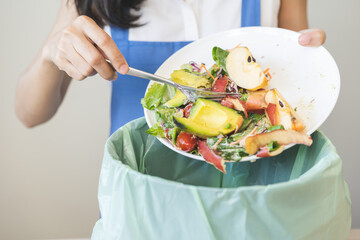 Compost from leftover food asian young housekeeper woman, female hand holding salad bowl use fork scraping waste, rotten vegetable throwing away into garbage, trash or bin. Environmentally responsible