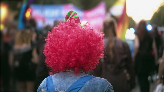 Person wear pink clown wig. Dressed up man enjoy joy festival. Fancy carnival hat. Happy jester have fun child party. Red colorful curly hair. Cute buffoon costume. Comic fest outdoor. Festive show.