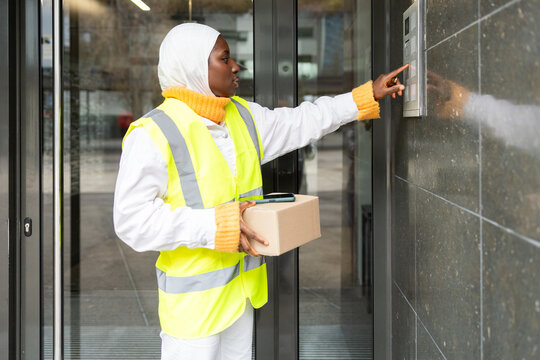 Delivery Woman in Hijab Presses Buzzer While Holding Package