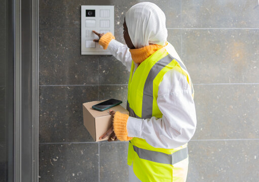 Delivery woman in hijab ringing doorbell