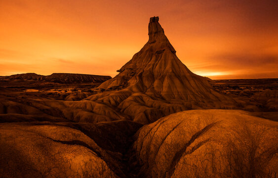 An awe-inspiring badlands spire stands tall under a fiery sunset sky, with intricate erosion patterns sprawling across the foreground