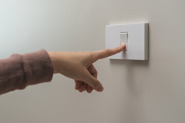Close up of hand of woman turn off on lighting switch at home room. Finger pushing light switch turn on or off white switch on wall for saving, control power electrical energy, eco environment concept - obrazy, fototapety, plakaty