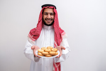 arabic man holding plate of maamoul represnets hospitality and genouresty weraring kandoura with keffeyeh on isolated white background for eid celebrations .