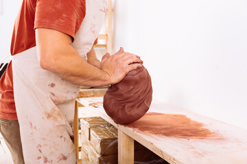 Crop of anonymous young man kneading clay on workbench in pottery studio