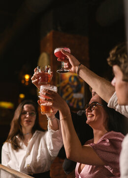 Happy people cheers glasses with cocktails celebrating event in bar. Joyful friends raise up drinks at party in night club