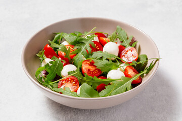 Fresh green salad made with mozzarella cheese, cherry tomatoes, arugula and olive oil on white stone table background. Healthy food and diet concept.