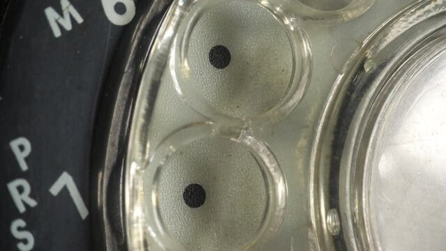 Making a telephone call on a rotary dial landline telephone. Close up of dialling with a pencil rubber end on a rotary dial telephone.