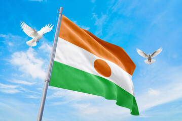 Waving flag of Niger in beautiful sky and flying pigeons. Niger flag for independence day. The symbol of the state on wavy fabric.