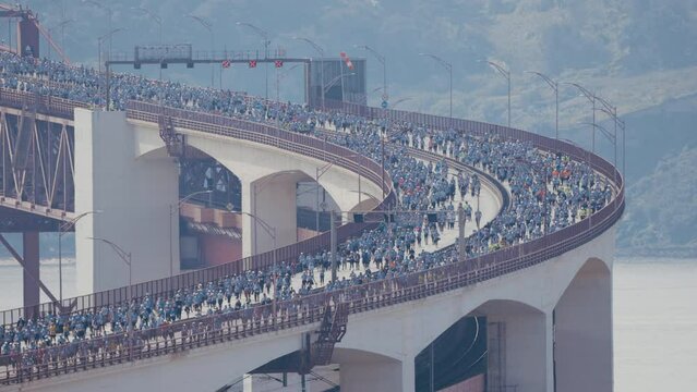 Running Lisbon half marathon crossing the 25 of April bridge over the Tagus river aerial view from above. Big crowd moving down the bridge from start to finish. Curved part of the road. Sunny day